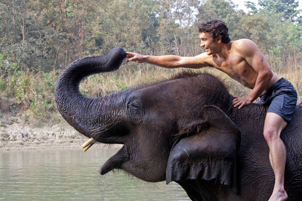 Biggest & Baddest star Niall McCann at the river with his domestic elephant in Nepal. A supreme athlete and biologist, Niall is James Bond/Tarzan and Indiana Jones rolled into one. He will ride this elephant into the jungle to discover huge rare prehistoric-looking Asian elephants.