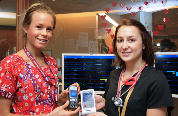 Robyn Mauro (right) holds the portable telemetry unit, which allows patients to be monitored away from their beds. Information appears on the screens (background) at the nurses’ station. Riley Burgsteden shows a special phone that alerts nurses on rounds if there is a problem with a patient.