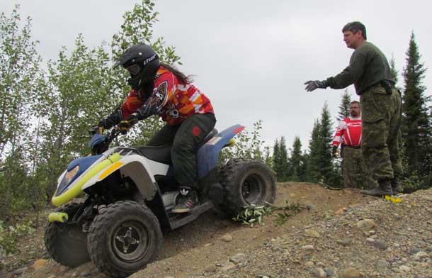 A Junior Canadian Ranger drives an all-terrain vehicle down a sharp incline at Camp Loon under the watchful eye of a Canadian Army instructor.