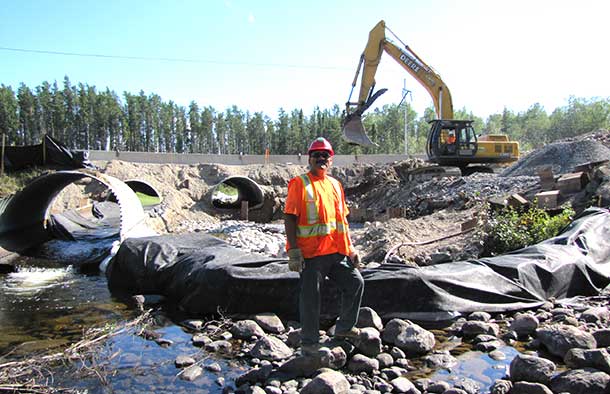Darren Bananish stands in the bed of Creelman Creek.  Behind him the culvert upgrade project proceeds apace.