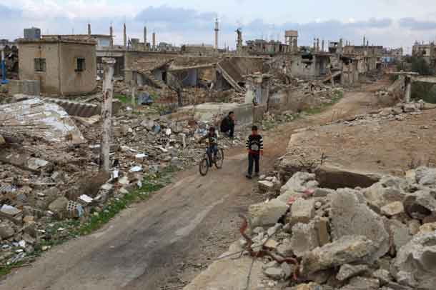 A boy rides a bicycle past a man sitting on rubble of a damaged house in the rebel held historic southern town of Bosra al-Sham, Deraa, Syria February 23, 2016. REUTERS/Alaa Al-Faqir