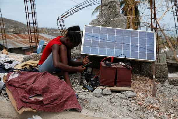 A woman looks at her mobile phone as it charges through solar panels after Hurricane Matthew passes in Jeremie, Haiti, October 9, 2016. REUTERS/Carlos Garcia Rawlins