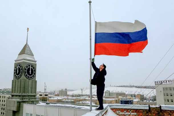 A worker lowers the Russian national flag to half-mast on a roof of the city administration building, as the country observes a day of mourning for victims of the Tu-154 plane which crashed into the Black Sea on its way to Syria on Sunday, in Krasnoyarsk, Russia, December 26, 2016.  REUTERS/Ilya Naymushin
