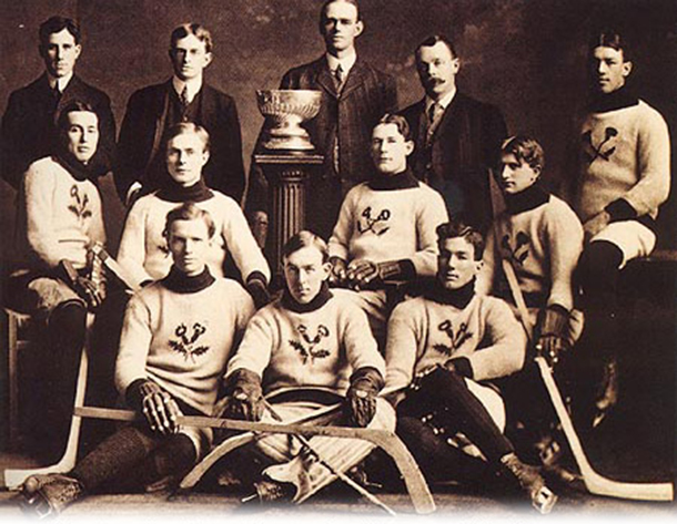 The Kenora Thistles’ Stanley Cup championship photograph.  Back row: team president Lowry Johnson, Russell Phillips, coach and trainer  J. A. Link, and team manager Red Hudson.   Middle row: Roxy Beaudro, Tom Hooper,  Tommy Phillips, Billy McGimsie, and Joe Hall.   Front row: Si Griffis, Eddie Giroux, and Art Ross.