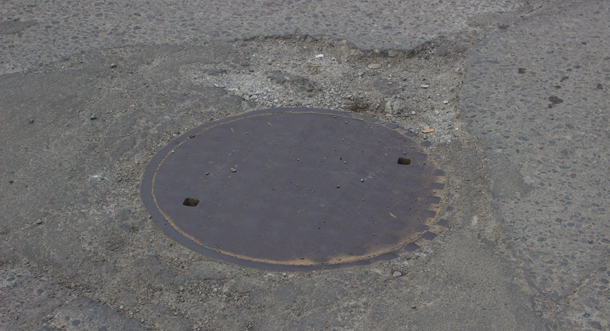Potholes form and bust up our roads. Here is one where the manhole is too high to drain.
