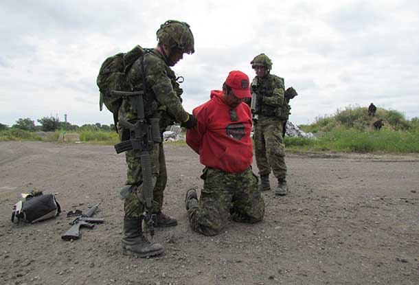 Master Corporal Leslie Anderson of Kasabonika kneels as soldiers take him prisoner.