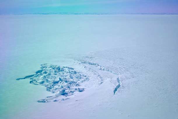 In April 2014, researchers flew over a site in southwest Greenland to find that a sub-glacial lake had drained away. This photo shows the crater left behind, as well as a deep crack in the ice. Credit: Photo by Stephen Price, Los Alamos National Laboratory, courtesy of The Ohio State University.