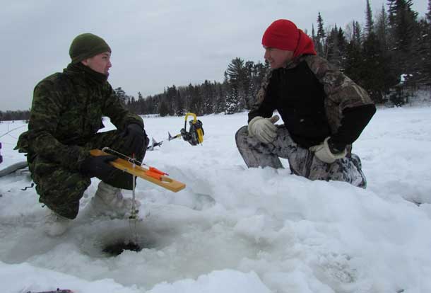 Corporal Benjamin Stephenson gets useful hints on ice fishing from Ranger Brandon Nakogee