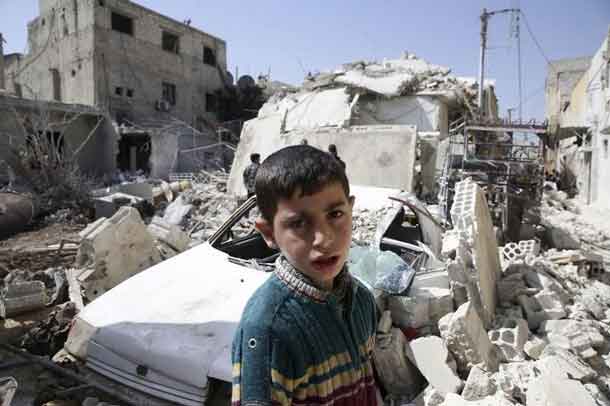 A boy looks on while residents inspect a damaged building in the rebel held besieged city of Douma, a suburb of Damascus, Syria February 27, 2016. REUTERS/Bassam Khabieh