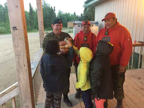 Warrant Officer Barry Borton, an army instructor, plays with a local puppy while talking to children in Wapekeka with Canadian Ranger Master Corporal Jacob McKay, centre, and Sergeant Spencer Anderson, right.  Credit: Lieutenant-Colonel Matthew Richardson, Canadian Rangers