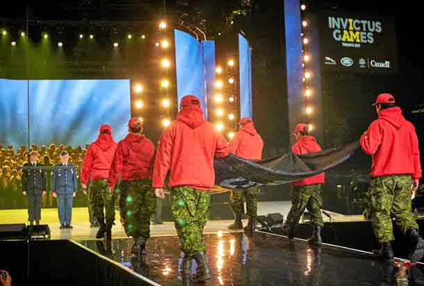 Canadian Rangers carry the Invictus Games flag across the arena floor to the stage.