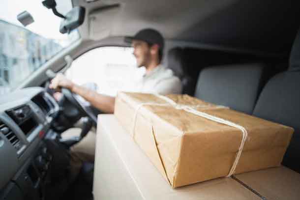 Delivery driver driving van with parcels on seat outside the warehouse - Image Depositphotos.com