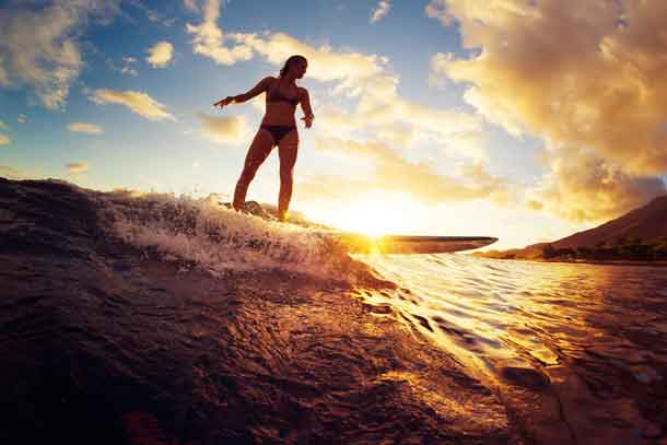 Surfing at Sunset. Beautiful Young Woman Riding Wave at Sunset. Image by Depositphotos.com