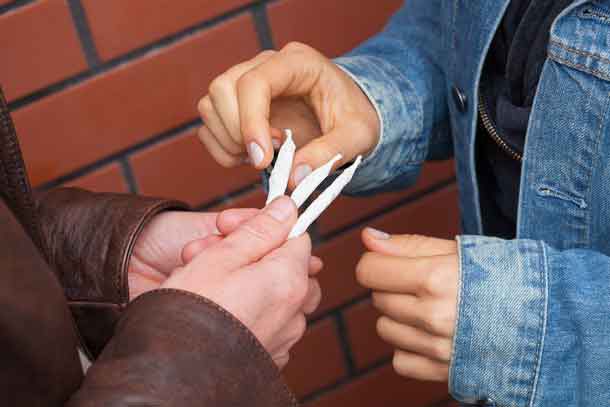 Student in brown jacket giving joint to colleague