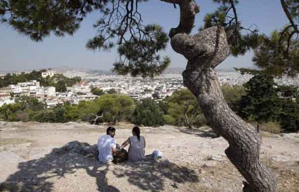 Archive Photo: Tourists sit under a pine tree on a hill overlooking Athens July 7, 2011. REUTERS/John Kolesidis