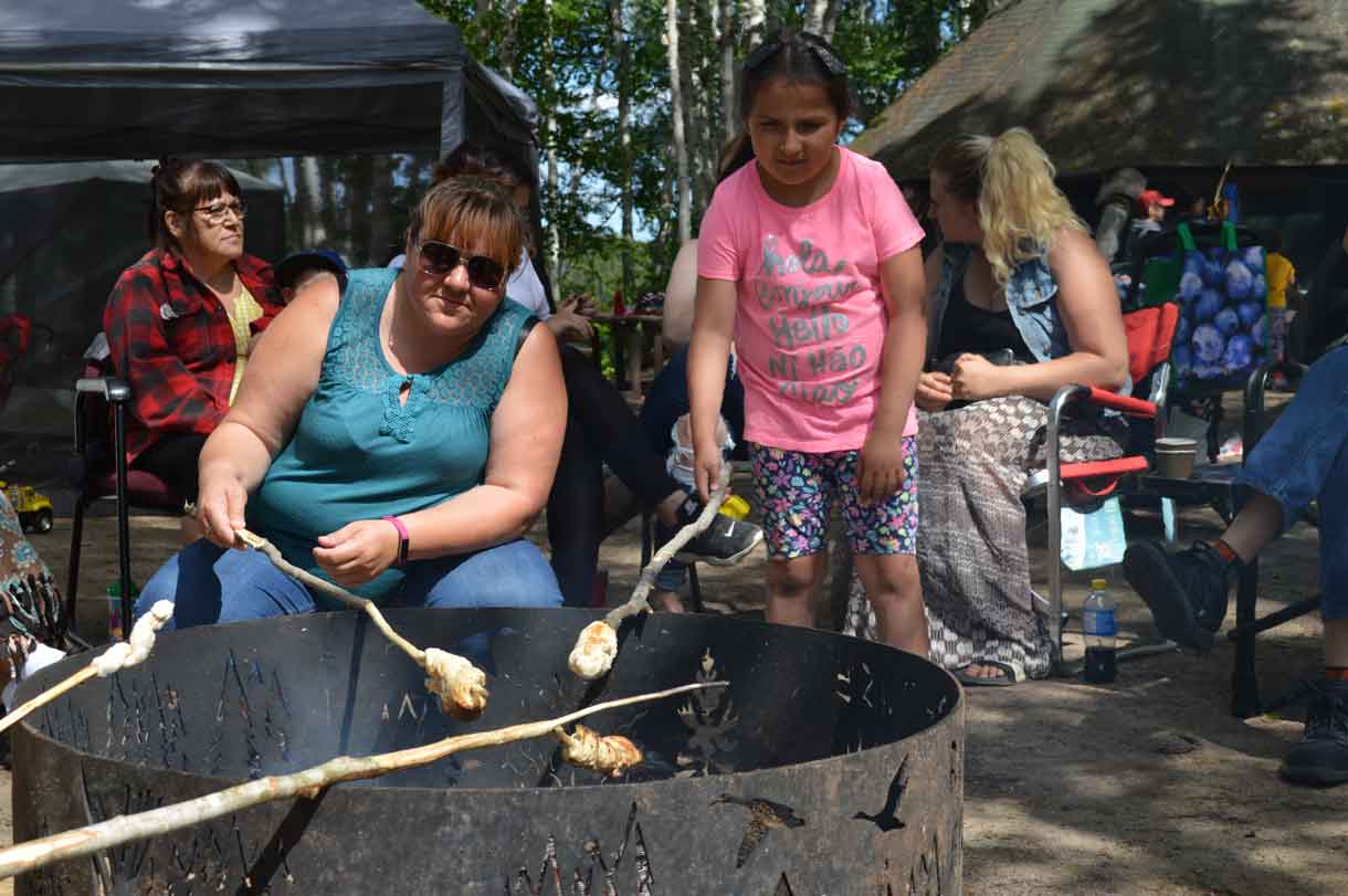 Traditional activities included making bannock at the Indigenous Language Gathering at Dorothy Lake on July 6 and 7. Here we see Amanda Julien, Matachewan FN showing Payton Batisse how to roast bannock over a fire. 