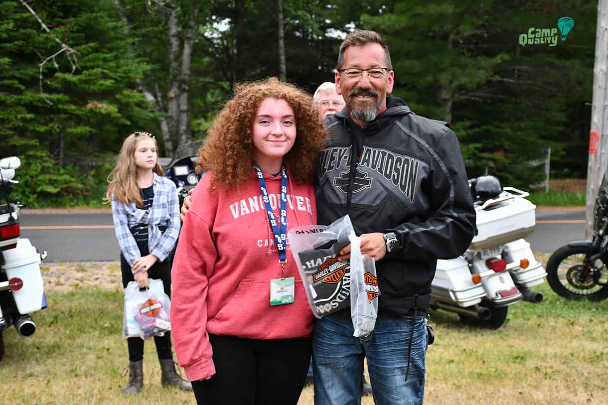 Camper Isabella posing with biker Trent after receiving her Harley Davidson t-shirt.