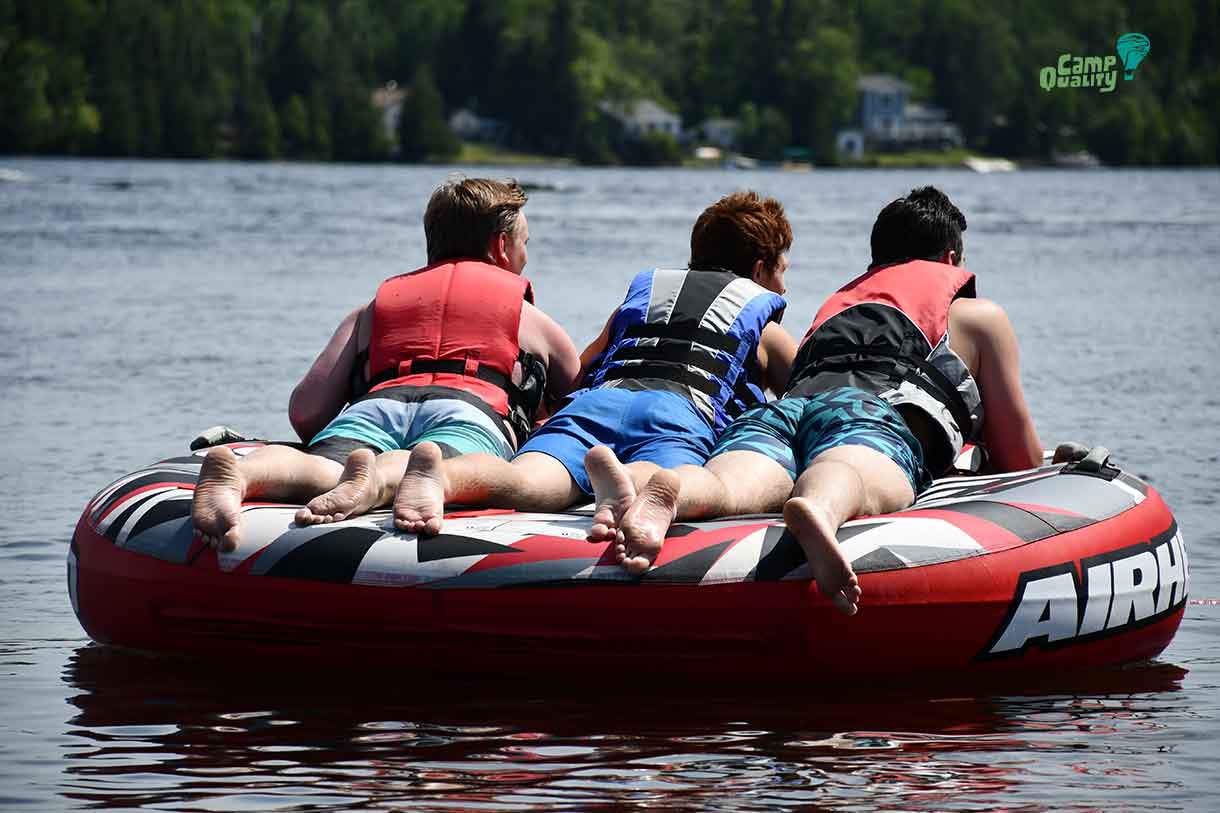 (from left) – Volunteer Braeden, camper Zeke and volunteer Brady taking a spin on the tube!