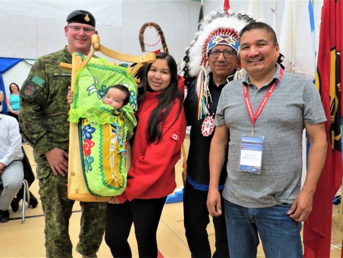 New Canadian Ranger Shawnda Mamakwa holds her son, Ashton, two months, in a traditional Oji-Cree cradleboard. She is flanked, from left, by Lieutenant-Colonel Matthew Richardson, Grand Chief Alvin Fiddler, and Kingfisher Lake Chief Eddie Mamakwa. - Image Sgt Peter Moon
