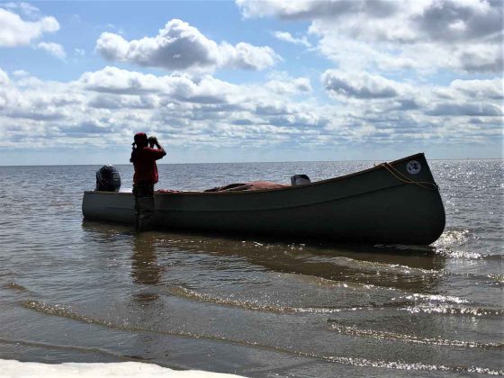 Sergeant Thomas Scott of Fort Albany First Nation uses binoculars to see how far the tide has gone out on James Bay.