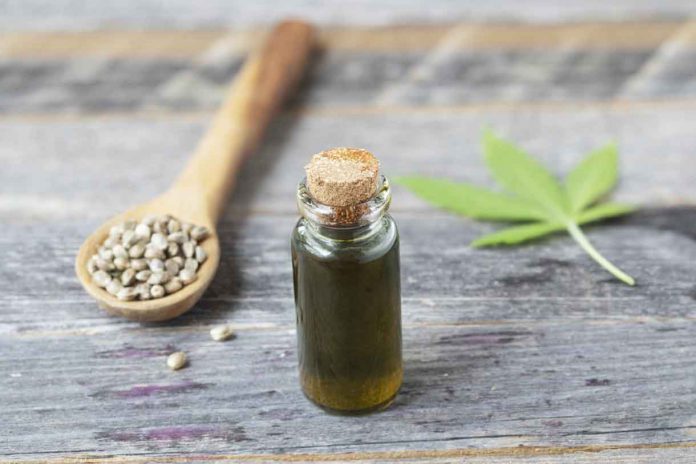 Small bottle of CBD oil with cannabis leaf and seeds in a wooden spoon.