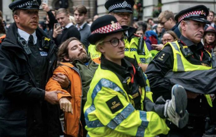 Police officers remove a volunteer with the Extinction Rebellion who was protesting the role of banks in financing fossil fuel projects undermining the 2015 Paris Agreement to curb climate change, in London, Britain, October 14, 2019, in this image obtained via social media. Louise Jasper via REUTERS