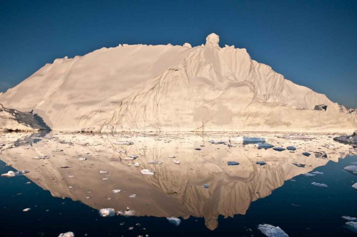 The midnight sun casts a golden glow on an iceberg and its reflection in Disko Bay, Greenland. Much of Greenland's annual mass loss occurs through calving of icebergs such as this. - CREDIT Ian Joughin, University of Washington