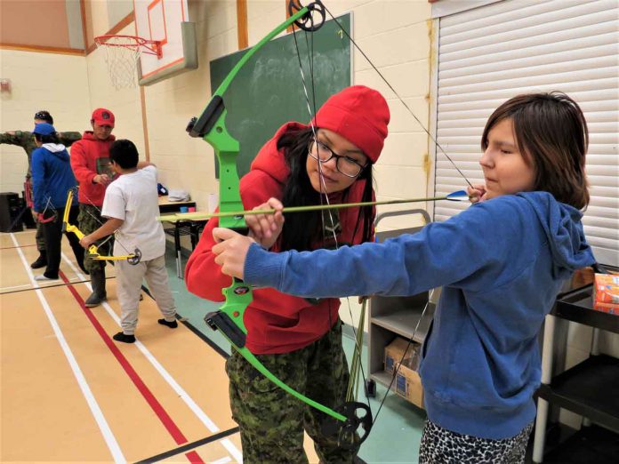 Ranger Nadine Strang of Pikangikum First Nation helps a girl using a bow and arrow for the first time in North Spirit Lake First Nation