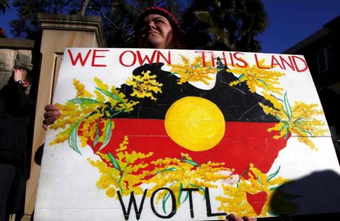 FILE PHOTO - A protester holds a placard as she stands outside the venue for a meeting between Australia's Prime Minister Tony Abbott and forty of the nation's most influential Indigenous representatives in Sydney, Australia, July 6, 2015. REUTERS/David Gray