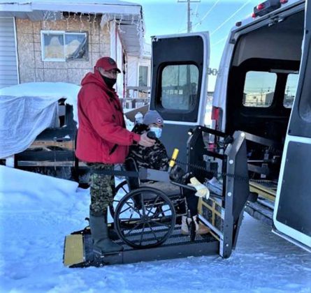 Corporal Dennis Sutherland helps an elder in Kashechewan into a wheelchair accessible vehicle to take her to the vaccination site. credit Sergeant John Sutherrland, Canadian Rangers