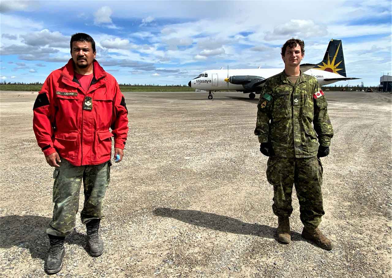 Master Corporal Joe Lazarus of the Canadian Rangers, left, and Master Corporal Jason Lane at the Kashechewan airport. A cargo plane bringing in food and supplies for the residents of the First Nation is behind them. credit Sergeant Janet Butt, Canadian Rangers