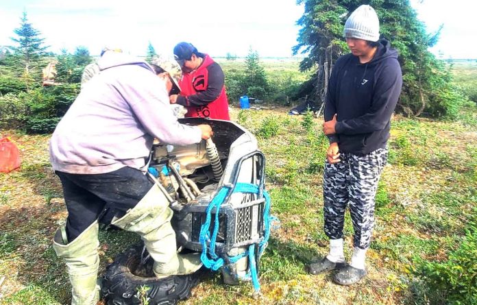 Stranded hunter Zachary Kakekaspan, right, watches as his rescuers repair his ATV engine. credit Sergeant Christopher Koostachin, Canadian Rangers