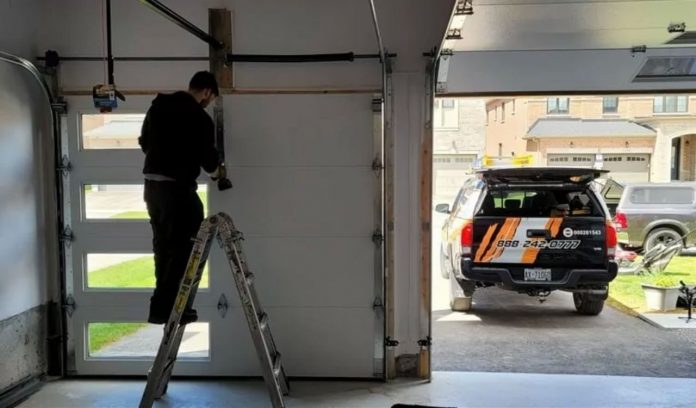 A handyman fixing a roll-up garage door while standing on a ladder