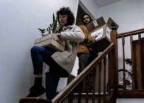 A-couple-is-moving-out-of-their-apartment,-carrying-boxes-and-plants