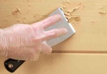 8 Costly Mistakes Homeowners Make When Hiring Painters Gloved hand scrapes wall to remove imperfections, highlighting why surface prep is crucial for interior painting success.