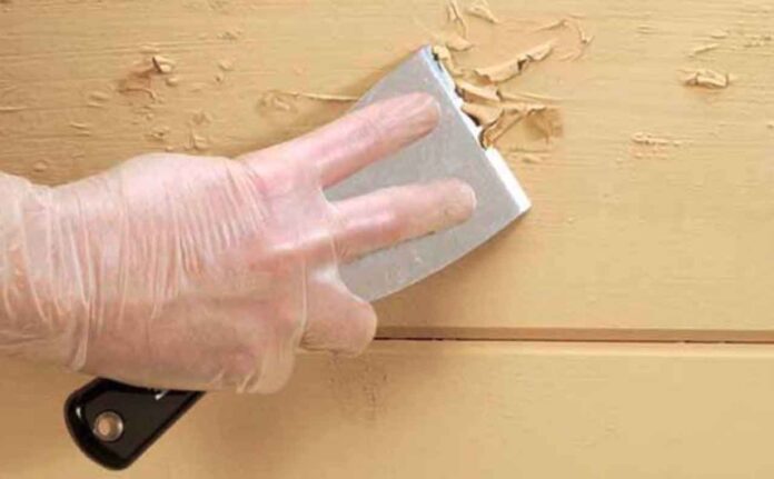 Gloved hand scrapes wall to remove imperfections, highlighting why surface prep is crucial for interior painting success.