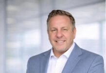 Jody Humphrey Redefines the Role of Financial Education in Today’s Economy Professional man in a light blue blazer and white shirt posing confidently in a bright office hallway, hands in pockets.