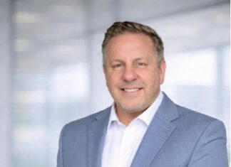 Jody Humphrey Redefines the Role of Financial Education in Today’s Economy Professional man in a light blue blazer and white shirt posing confidently in a bright office hallway, hands in pockets.